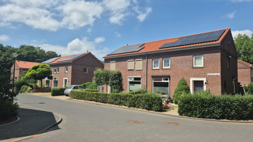 Rij bakstenen woningen met rode dakpannen en zonnepanelen op de daken in een rustige woonwijk op een zonnige dag
